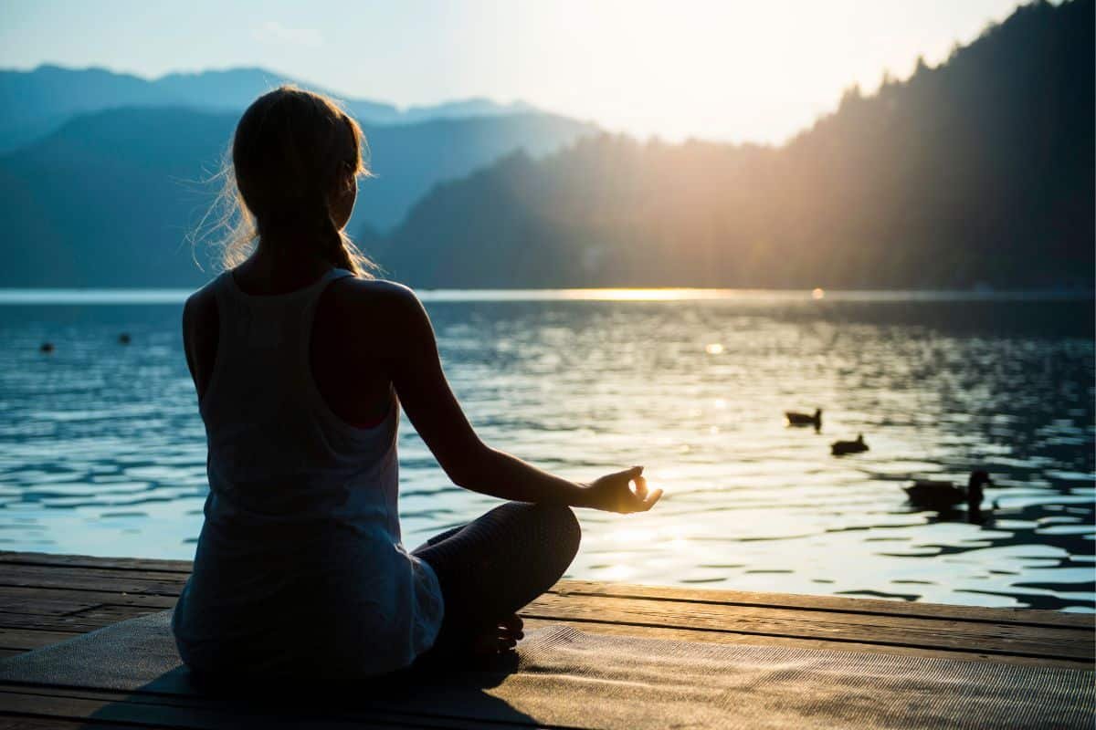 a woman meditating by a lake