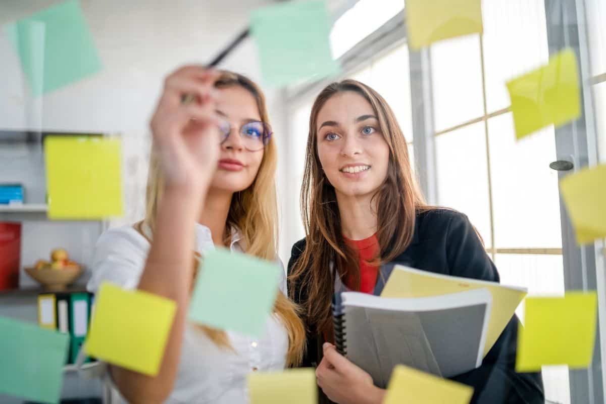 two woman looking at a board of tasks