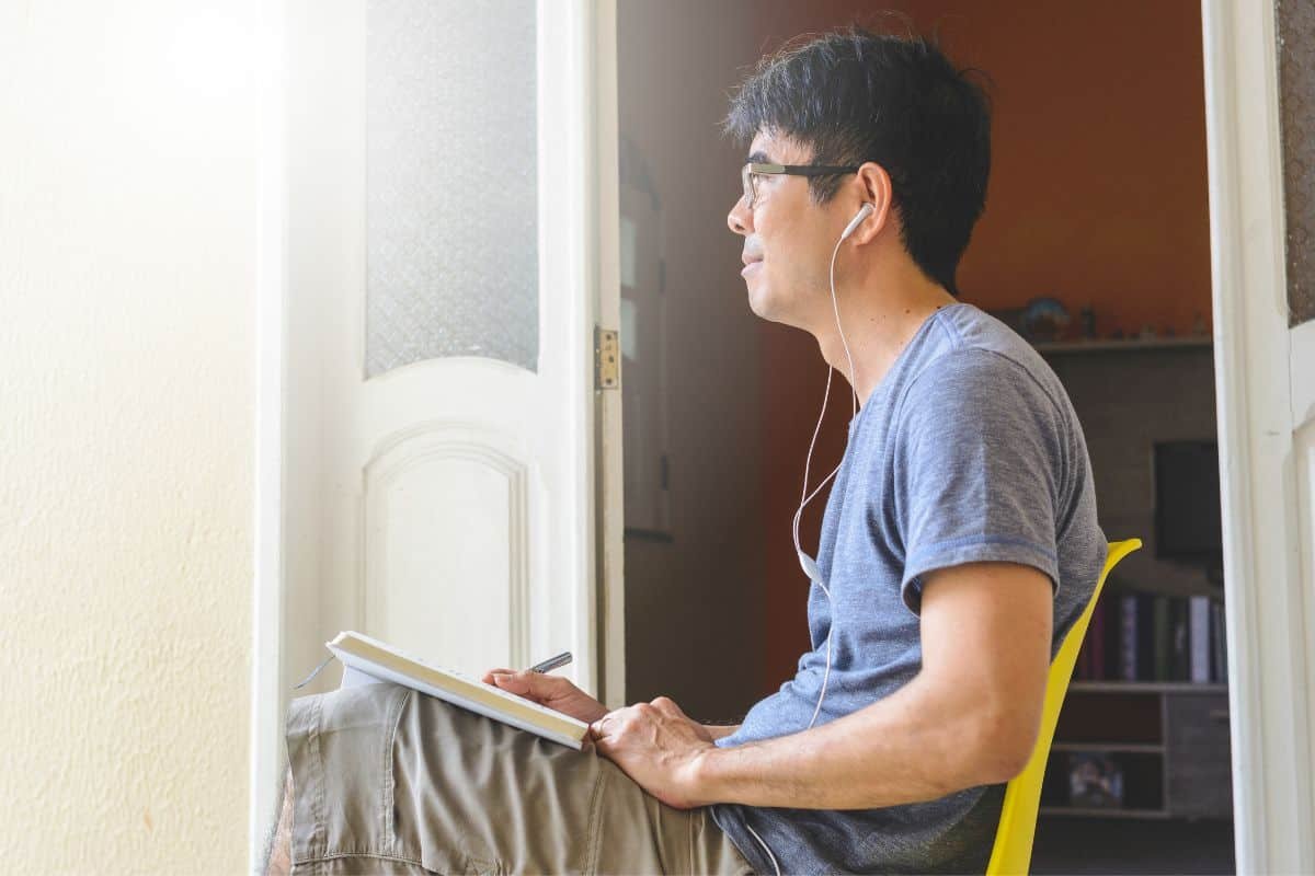 a man sitting with earphones and writing in a book