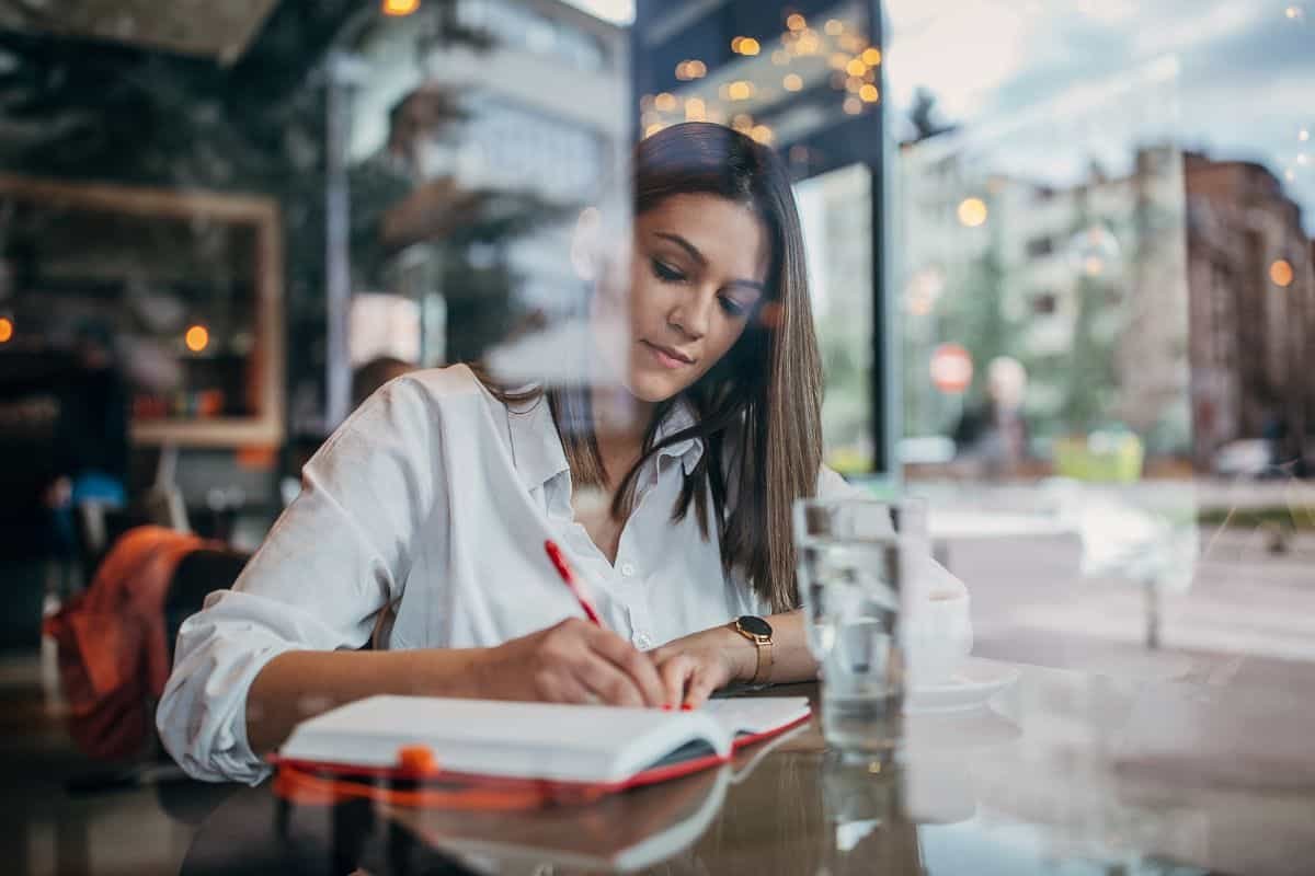 female author writing in a book through a window