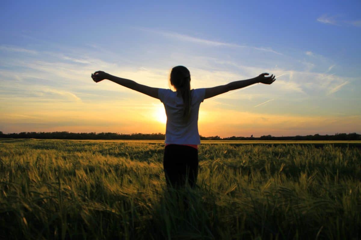 girl standing in a field with the sunsetting