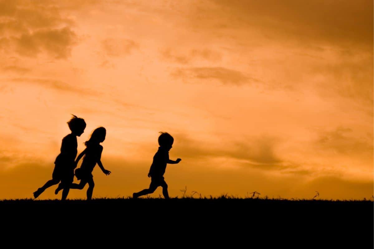 three children silhouette running on grass